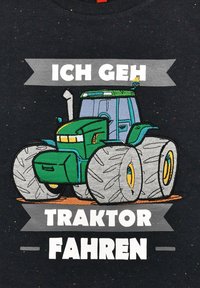 Schwarzes T-Shirt mit einer grünen Traktorillustration und übergroßen Reifen, geprägt mit dem Text: "Ich geh Traktor fahren" und multicolorigen Sprenkeln.