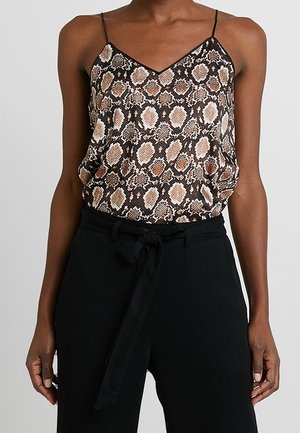 Woman wearing a sleeveless snake print camisole with thin straps tucked into high-waisted black pants with a tied fabric belt.