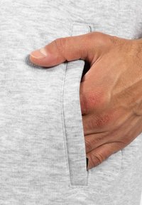 Šedá bavlněná tkanina má boční kapsu s viditelným švem. Ruka je umístěna uvnitř kapsy, což ukazuje texturovanou pokožku.