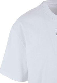 T-shirt en coton blanc à manches courtes, col rond et texture lisse. Présente un petit motif graphique noir sur le devant.