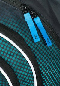 Černá a tyrkysová tkanina s potiskem a síťovými oblastmi, s modrými stahovacími zipy a kontrastními bílými detaily. Viditelný podrobný šev.