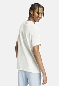 Camiseta blanca de algodón con mangas cortas, corte relajado, cuello redondo y una textura suave. Se lleva con pantalones azul claro.
