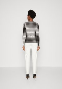 Top a righe bianco e nero a maniche lunghe con un design aderente, abbinato a pantaloni bianchi e scarpe con tacco nero. Look semplice e moderno.