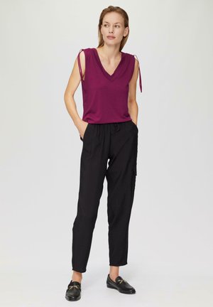 Haut en V violet foncé avec des nouettes aux épaules, associé à un pantalon noir léger et ample, et des mocassins noirs avec des accents dorés.