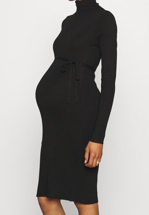 Gravid person iført en tætsiddende sort langærmet kjole med rullekrave og bælte bundet over maven.