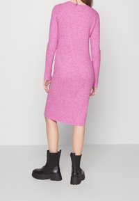 Långärmad, ribbad stickad klänning i starkt rosa, knädlång, med sidosprund och rund halsringning. Samlad med kraftiga svarta ankelskor.