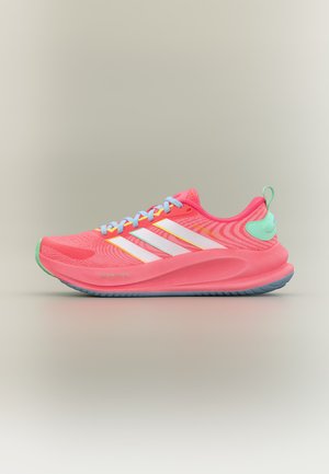 Chaussure de sport rose vif avec des bandes blanches, des lacets bleu clair, un renfort de talon vert et une semelle épaisse et rembourrée sur fond neutre.