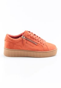 Baskets en daim orange avec une semelle plateforme texturée marron, présentant un détail de fermeture éclair sur le côté et un laçage à l'avant.