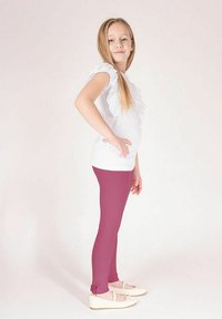 Biała koszulka z falbankami na rękawach w połączeniu z fioletowymi legginsami. Legginsy mają gładką teksturę i sięgają tuż nad jasne baleriny.