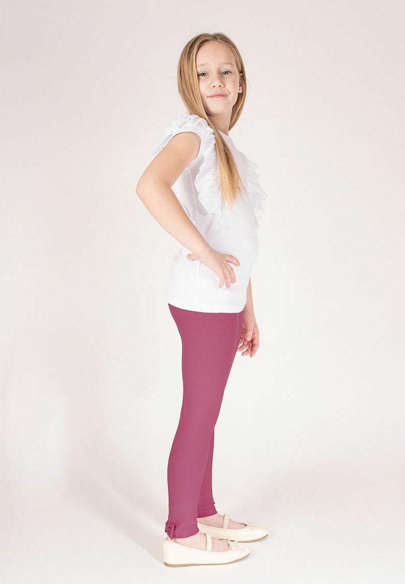 Biała koszulka z falbankami na rękawach w połączeniu z fioletowymi legginsami. Legginsy mają gładką teksturę i sięgają tuż nad jasne baleriny.