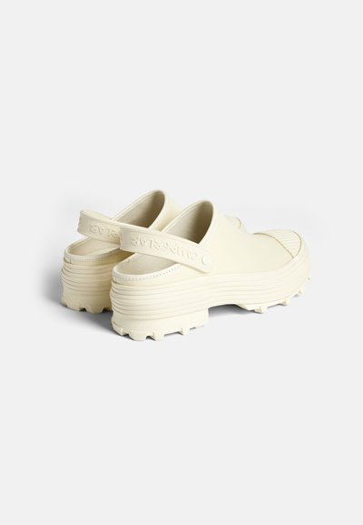 Crème-kleurige instap schoenen met een dikke, gegroefde zool en achterband. Gemaakt van flexibel materiaal met een gestructureerde afwerking.