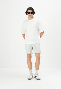Camiseta de algodón blanca, pantalones cortos a rayas azul claro, calcetines grises, gafas de sol negras y zapatillas negras/blancas. Diseño minimalista, ajuste casual.