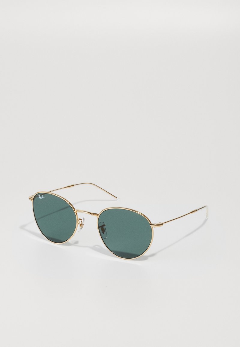 Occhiali da sole con montatura in metallo dorato e lenti ovali verde scuro, con stanghette sottili e dettaglio del logo sulla lente sinistra. Design minimalista senza decorazioni.