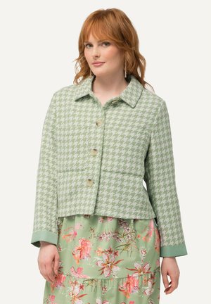 Vihreä houndstooth-kuvioitu lyhyt takki, jossa on kaulus, etutaskut ja nappikiinnitys. Pitkät hihat, joissa on kontrastiväriset hihansuut.