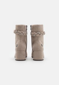 Bottines en suède beige avec un design tressé à la cheville, fermeture éclair et un talon empilé. Texture lisse avec un petit détail de logo.