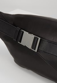 Marsupio in pelle nera con una texture liscia, dotato di una fibbia in metallo argentato. Design compatto con una tracolla regolabile.