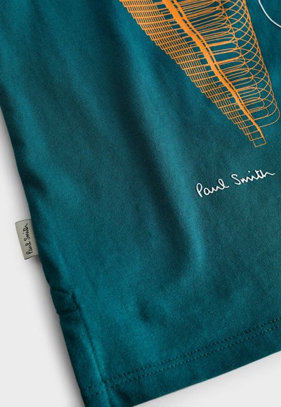 Teal bomullströja med en orange grafisk design och vit text. Har en sydd fåll och en etikett som visar "Paul Smith."
