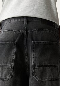 Shorts in denim nero con un taglio dritto, due tasche posteriori e un design semplice della vita. Il tessuto ha un aspetto leggermente testurizzato.