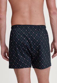 Zwarte bokser shorts met een geometrisch patroon in rood en wit, gemaakt van zachte stof met een elastische tailleband voor comfort.