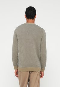 Pulôver de malha em padrão de houndstooth beje e preto, com decote redondo e punhos e bainha canelados. Tecido leve com design texturizado.