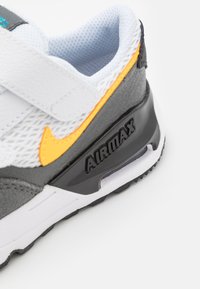 Sneaker bianco e grigio con materiali in rete e suede, logo Nike arancione, suola in gomma nera e unità di ammortizzazione visibile.