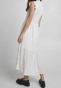 Biała midi sukienka z marszczonym gorsetem i falbaniastymi rękawami. Posiada składający się z warstw dół oraz fakturowany materiał. Zestawiona z masywnymi czarnymi butami.