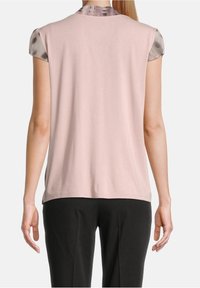 Haut rose clair à manches courtes avec une texture lisse et un col à motifs contrastants. Porté avec un pantalon noir, mettant en avant une coupe décontractée.