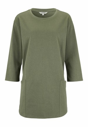 Grøn langærmet tunika med rund halsudskæring og to forlommer, vist mod en hvid baggrund.