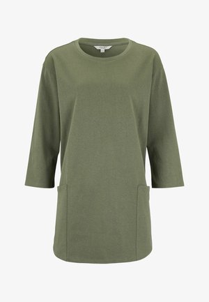 Grøn langærmet tunika med rund halsudskæring og to forlommer, vist mod en hvid baggrund.