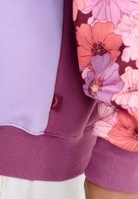 Helelilla ja tume burgundia värvi dressipluus lillemustriga, soonikkoes varrukate ja alläärega, külje peal oleva väikese sildiga.