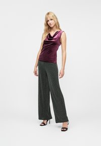 Burgundin samettinen hihaton toppi, jossa on laskeutuva kaula-aukko, yhdistetty leveälahkeisiin, teksturoituihin mustiin housuihin, viimeistelty avonkulkeneilla mustilla korkokengillä.