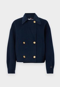 Σακάκι διπλής όψης ναυτικού μπλε από μάλλινο υλικό με χρυσά κουμπιά, επεκταμένο γιακά, μακριά μανίκια και μικρή κεντημένη λογότυπο στον καρπό.