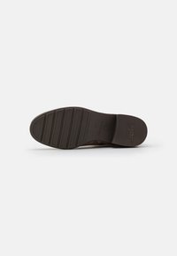 Suela de zapatilla marrón con una superficie de goma texturizada, que presenta surcos horizontales y una impresión de logo. Diseñada para agarre y durabilidad.