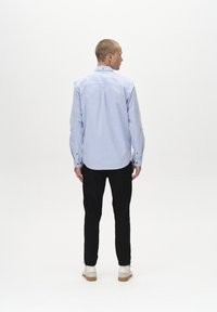 Light blue button-up shirt with a back yoke, long sleeves, and contrasting buttons; paired with black pants and white sneakers.
