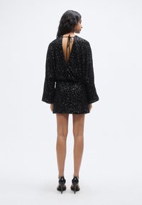 Μαύρο φόρεμα με παγιέτες, που διαθέτει βαθύ V στην πλάτη, μακριά μανίκια καμπάνα και εφαρμοστή μέση, συνδυασμένο με μαύρες ψηλοτάκουνες γόβες.