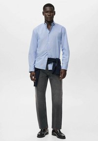 Light blue striped button-up shirt paired with dark gray straight-leg jeans. A navy sweater is tied around the waist. Black shoes complete the look.