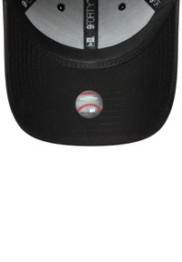 Boné de baseball preto com uma aba plana e um adesivo prateado redondo apresentando um gráfico de baseball na parte da frente. O interior é cinzento.