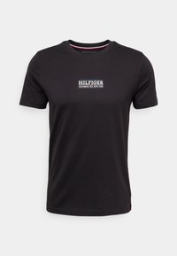 Černé tričko s krátkým rukávem vyrobené z bavlny. Na hrudi má bílé logo s nápisem "HILFIGER COLUMBUS AVE. NEW YORK". Jednoduchý kulatý výstřih.