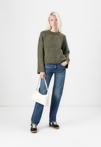 Olive zielony sweter dzianinowy o luźnym kroju, niebieskie dżinsy, czarne sneakersy z białymi akcentami oraz biała torebka z detalem w postaci sznurówki.