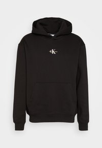 Sudadera negra hecha de una mezcla de algodón, con un bolsillo frontal, puños y dobladillo acanalados, y un pequeño logo blanco en el pecho.