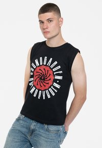 Black sleeveless T-shirt featuring a bold red spiral graphic and white text, paired with light-wash jeans. Casual cotton material.