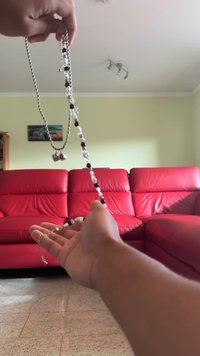 Zilveren ketting met afwisselend zwarte en witte kralen, met een sluiting. Een hand houdt de ketting boven een rode bank.