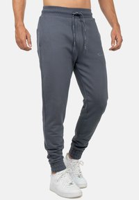 Grijze sweatpants met een elastische tailleband en trekkoord, voorzien van zijzakken en geribbelde boorden. Gecombineerd met witte sneakers.