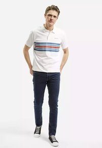 Biała koszulka polo w poziome niebieskie i czerwone paski, z krótkimi rękawami i kołnierzykiem. Połączona z ciemnymi dżinsami i czarnymi sneakersami.