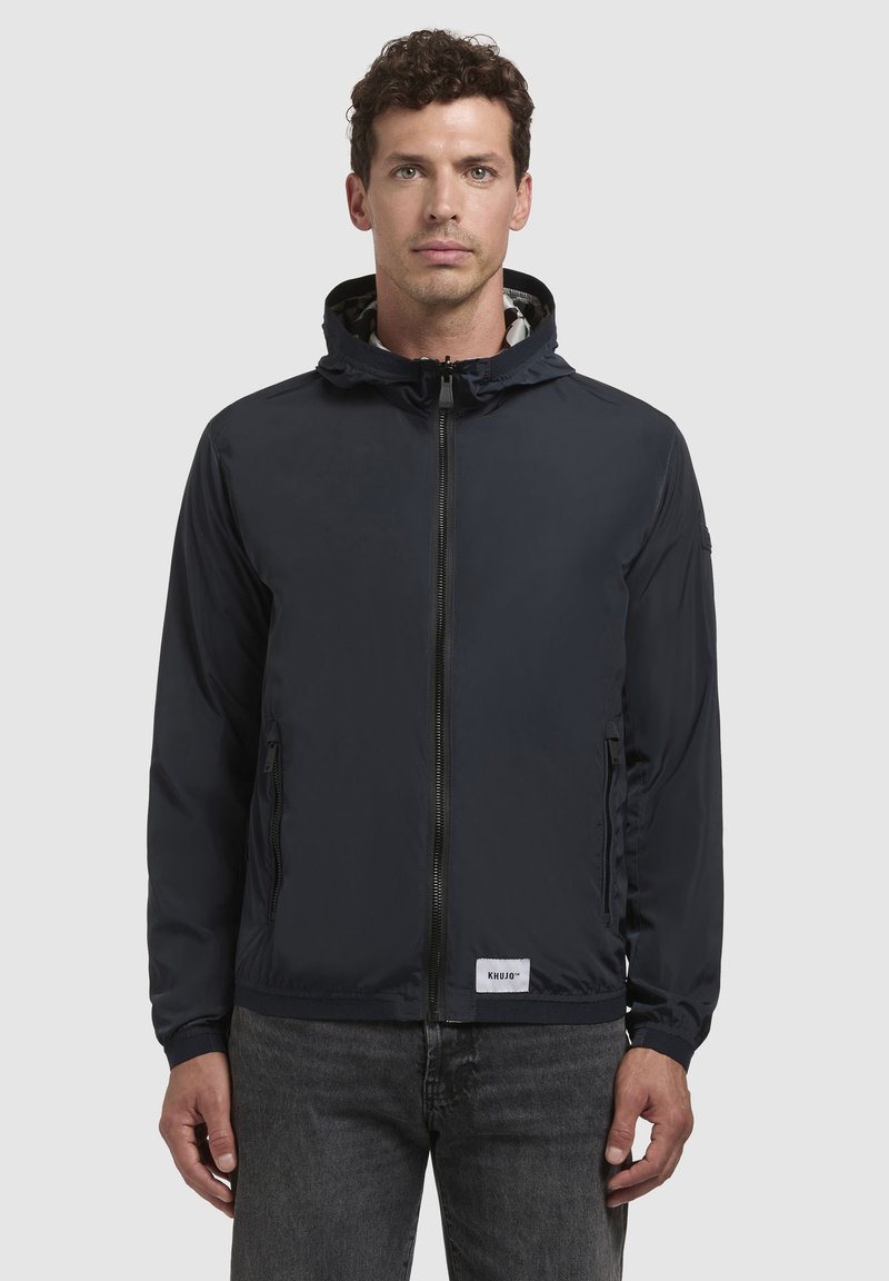 Marineblau leichte Jacke aus wasserdichtem Material mit einem Reißverschluss vorne, Kapuze mit Kordelzug und seitlichen Taschen; mit Markenlogo.