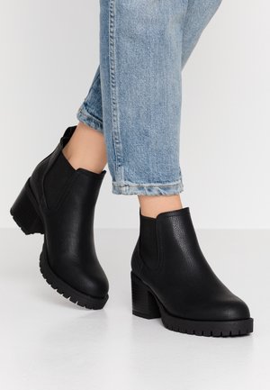 Sorte ankelstøvler med tekstureret overflade, elastiske sidepaneler og en blokhæl. Båret med opkrogede lyseblå jeans, der viser en afslappet stil.