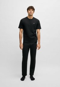 Zwarte T-shirt met korte mouwen en ronde halslijn, met een klein "BOSS" logo, gecombineerd met zwarte taps toelopende broek, tentoongesteld op een effen achtergrond.