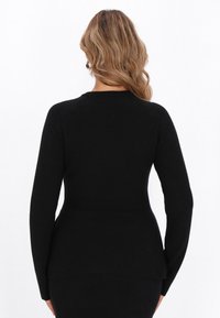 Musta pitkähiha istuva paita, jossa on pehmeä pinta, pyöreä kaula-aukko ja peplum-helma, joka tuo lisää muotoa. Saumadetaillia olkapäillä.