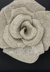 Rhinestones-szal díszített ezüst virág bross, rétegezett szirmokkal, fekete háttér előtt. Texturált felülettel és bonyolult részletezéssel rendelkezik.
