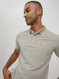 Hellgraues Poloshirt mit einem beigen Kragen, drei Knöpfen und einem kleinen weißen Logo auf der Brust. Es hat einen strukturierten Stoff und kurze Ärmel.